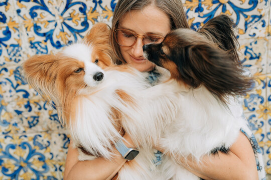 Woman embracing two fluffy Papillon dogs against patterned wall