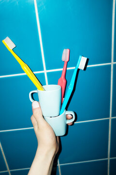 Hand holding porcelain cups full of colourful toothbrushes in bathroom