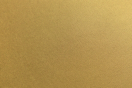 Gold leather texture close up. Abstract metallic leather background with realistic grain and soft golden shine. 