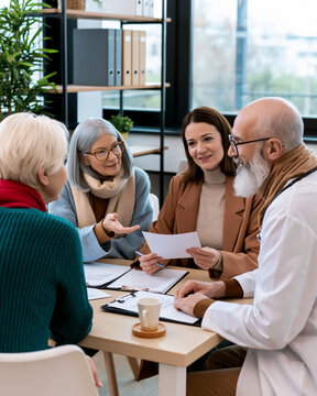 Senior patients consulting with healthcare professionals during medical meeting discussing treatment options insurance coverage and care planning in modern clinic environment