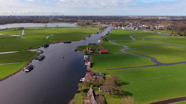 Aerial view of a river canal with houseboats and polder fields. Scenic drone panorama of green agricultural meadows, traditional houses, and waterways in the Netherlands countryside.