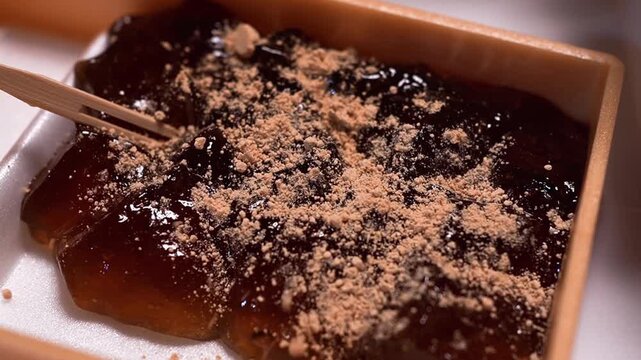 本蕨粉で作られた本格的なわらび餅にきな粉を振りかける瞬間のクローズアップ（和菓子動画素材）