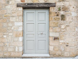 Fototapeta premium Pale grey wooden door framed by a rough stone wall in Athens, highlighting texture, craftsmanship, and timeless urban design.