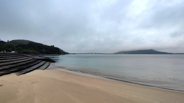 The sandy beach gradually turns into a stone embankment, with the sea and the bridge the background.