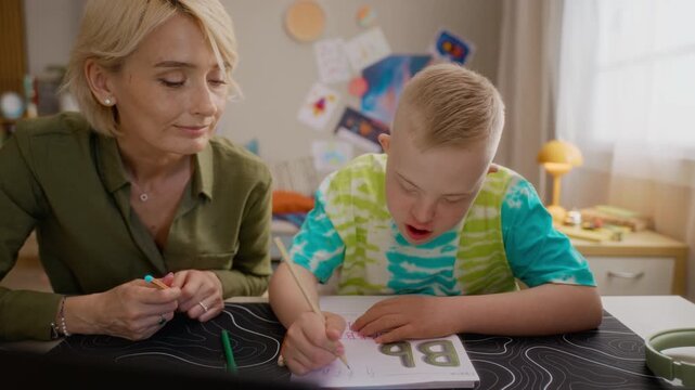 Mother and boy with Down syndrome practicing writing in notebook. Footage perfect for inclusive education and special needs marketing