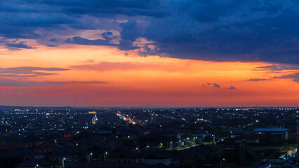 Fototapeta premium Panoramic view of a city skyline at dusk, with vibrant orange and blue hues in the sky and numerous lights illuminating the streets and buildings below