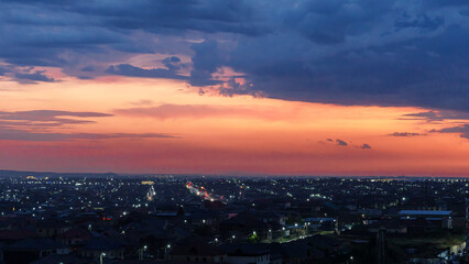 Fototapeta premium Panoramic view of a city skyline at dusk with illuminated buildings and streets under a colorful sunset sky filled with clouds