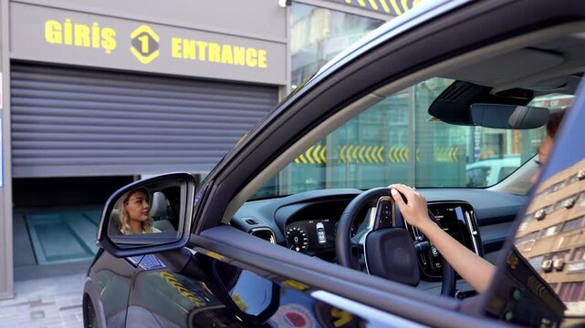 A female driver approaches a smart parking entrance by car. The side mirror detail and entrance sign show arrival at the parking system and everyday urban transportation.
