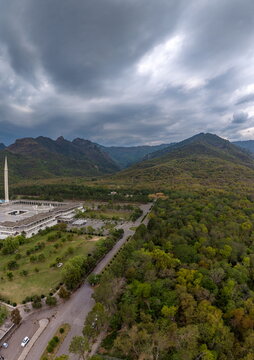 Aerial view of Faisal Masjid surrounded by lush green trees and the Margalla Hills under a cloudy sky in Islamabad, Islamabad Capital Ter, Pakistan.