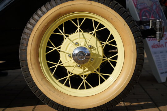 Direct closeup detail of  100-year-old 1929 Ford Model A antique car's wheel, featuring yellow painted wire spokes, chrome hubcap, and vintage whitewall tire Firestone, Subotica, Serbia, June 7, 2026