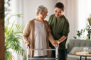 Fototapeta premium Caring Young Woman Assisting Senior Woman with Walker at Home