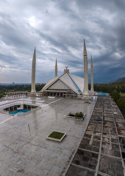 Aerial view of Faisal Masjid with its distinctive tent-shaped architecture and four slender minarets under a dramatic cloudy sky in Islamabad, Islamabad Capital Ter, Pakistan.