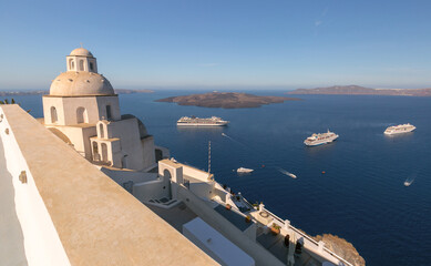 Obraz premium Whitewashed church dome overlooking the Santorini caldera with cruise ships anchored in the Aegean Sea.