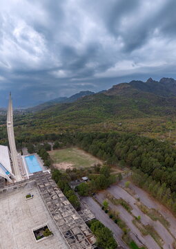 Aerial view of Faisal Masjid surrounded by lush greenery and the Margalla Hills under a dramatic cloudy sky in Islamabad, Islamabad Capital Ter, Pakistan.