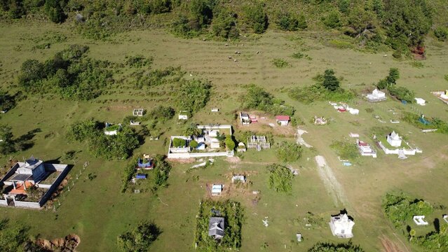 Aerial view of a cemetery with traditional Batak tombs scattered across a grassy hillside in Balige, North Sumatra, Indonesia.