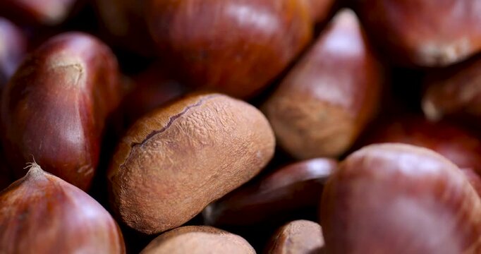 Dark chestnuts in a round container, these chestnuts have a smooth surface and are collected in a deep dish on a brown countertop background.