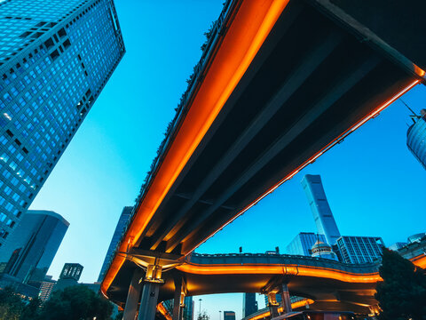 Scenic low angle view of the China Zun CITIC Tower and CBD skyscrapers behind a multilevel overpass illuminated by golden street light during blue hour at Guomao Bridge, Chaoyang, Beijing, China