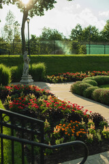 Obraz premium Decorative garden statue surrounded by colorful flower beds and manicured hedges in the Sunken Garden at Phillips Park Sunken Garden. Warm sunlight illuminates the formal garden pathways