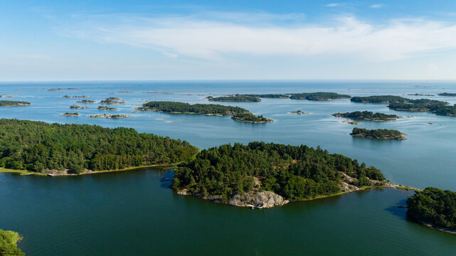 Aerial view of the Hiittinen archipelago with forested islands, rocky shores, and calm blue waters under a clear sky in Hiittinen, Southwest Finland, Finland.