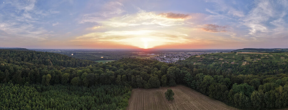 Aerial view of the town of Weingarten nestled among lush forests and agricultural fields during a vibrant sunset with a colorful sky in Weingarten, Baden-Wurttemberg, Germany.