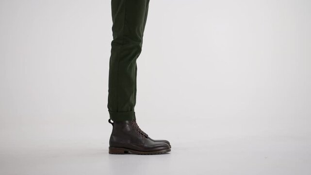 Man's legs in leather boots and green pants walking and stopping on an isolated white background