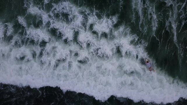 Aerial view from above with a 4K drone of a surfer doing a duck dive through a light green wave and the white of the foam create patterns in the sea of ​​San Marianita, Manta, Ecuador.