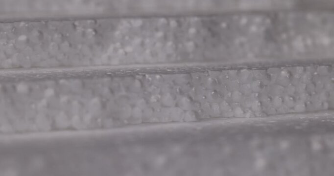 Embossed white foam with protrusions, this synthetic foam shows a cellular mass of small granules with shadows between the layers.