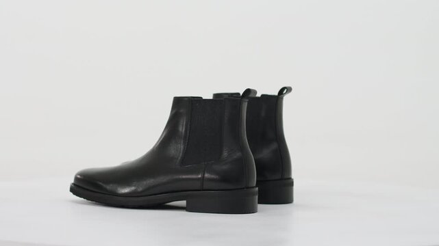 Black leather chelsea boots rotating on a turntable isolated on a white background for a fashion showcase