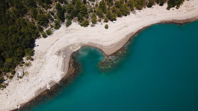 Aerial view of the turquoise waters of Lake of Sainte-Croix bordered by a sandy beach and pine forests in Provence-Alpes-Cote d'Azur, France.