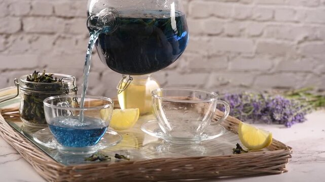 Butterfly pea flower tea is poured into a transparent glass cup. Fresh lemon juice is added to the blue herbal tea, creating a natural color transformation from blue to purple. Close-up footage of a h