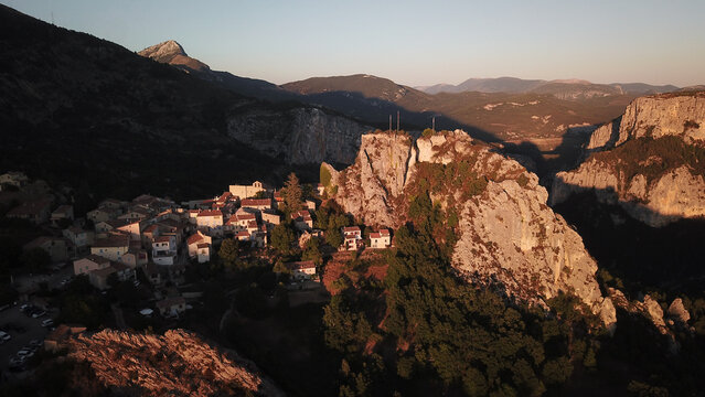 Aerial view of the village of Rougon near the Verdon Gorge limestone cliffs at sunset, with golden light on stone buildings and forest in Rougon, Provence-Alpes-Cote d'Azur, France.
