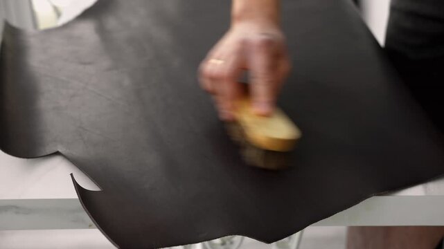 Leatherworker brushing a piece of dark genuine leather in a traditional workshop to prepare for crafting an accessory