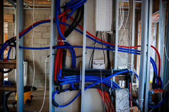 Riga, Latvia, winter renovation interior shows metal studs, brickwork, blue and red PEX with white cables, conduits, junction boxes, and a mounted distribution panel.