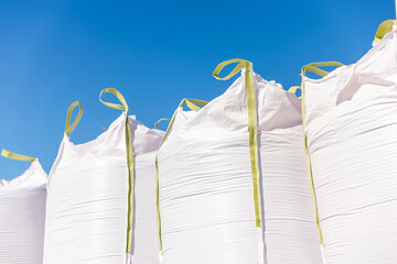 Oversized white super sacks with lime loops stand upright in rows under clear sky. Low angle view emphasizes height and uniform lines in bright midday light. © True Pixel Art