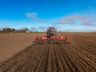 Fototapeta premium Wide angle view shows a tractor towing a seed drill cutting parallel furrows. Seed tubes and coulters are visible. Rural field, cool clear day, strong daylight.