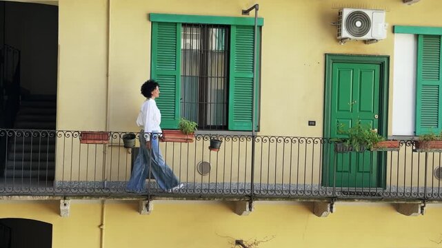 Woman Walks, Smells Flowers on Milan Balcony, Apartment Building