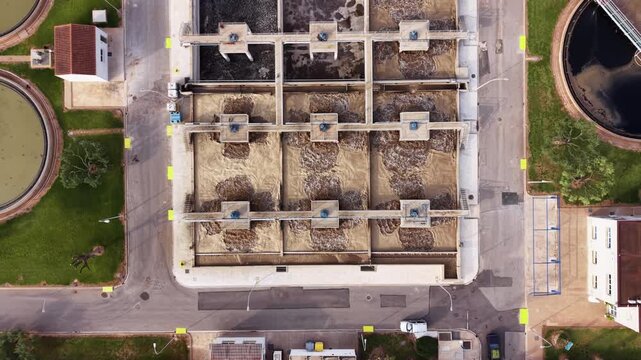 Top-down view of a modern wastewater treatment facility showing rectangular aeration basins with activated sludge, circular secondary clarifiers for sedimentation, and surrounding infrastructure