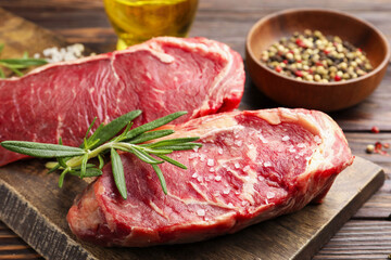 Fototapeta premium Raw beef steaks, spices, rosemary and oil on wooden table, closeup