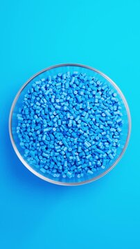 Rotating glass bowl filled with blue polypropylene plastic granules and masterbatch resin pellets on blue background, 3D render seamless Vertical video.