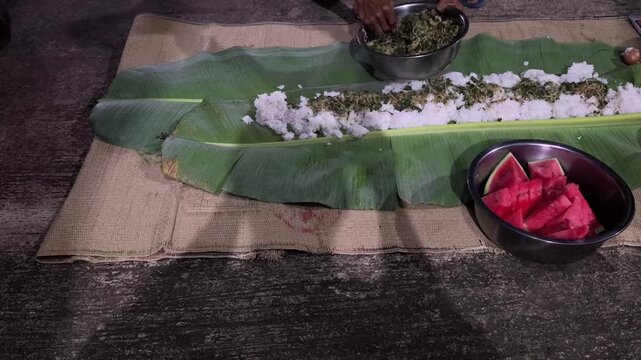 Traditional communal meal served on banana leaves featuring rice vegetables watermelon during gathering together.