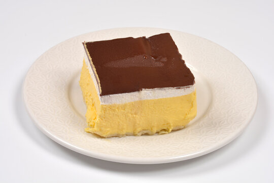 High angle view of a single square slice of traditional zagrebacka kremsnita cake with yellow custard whipped cream and chocolate glaze on a ceramic plate