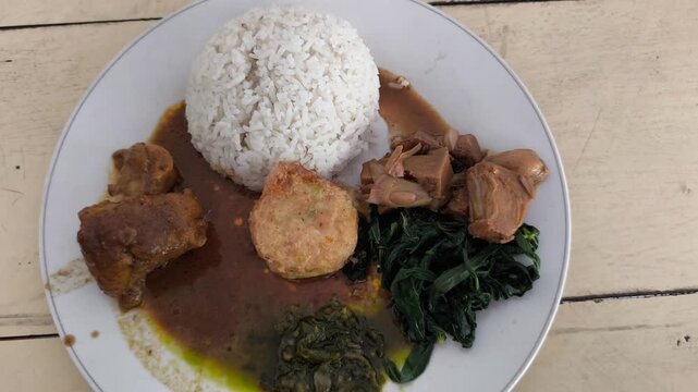 Traditional Indonesian rice meal featuring spicy curry chicken, vegetables, tofu, and jackfruit.