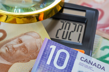 Plakat Horizontal close up of Canadian Dollar banknotes with calculator showing year 2027 and magnifying glass. Canada economic forecast, financial analysis, business background and currency concept