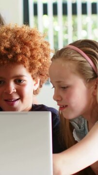 Vertical video: Pointing girl in pink headband tapping laptop at table, kids crowding to see screen
