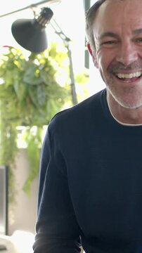 Vertical video: Smiling man in navy top at home on camera checking watch and laughing, copy space