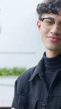 Vertical video: Smiling man turning and laughing after off-camera cue at plaza in tortoise glasses