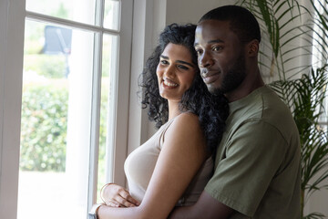 Obraz premium Indian woman wearing beige top with bracelet, African American man embracing near window at home