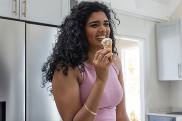 Adult Indian woman holding soft-serve cone, smiling in tank top, gold bracelets in home kitchen © wavebreak3