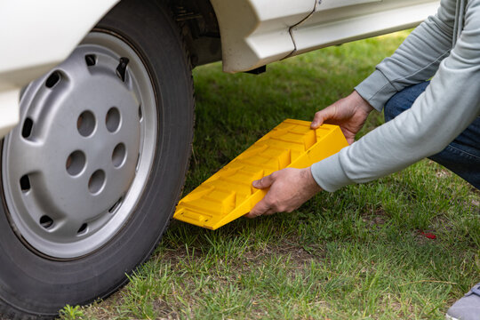Individual placing yellow wheel chock under tire of motor home on grassy surface, demonstrating vehicle stabilization for maintenance or parking purposes
