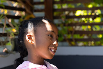 African American girl turning right smiling looking up wearing pink fleece on patio with trellis © wavebreak3